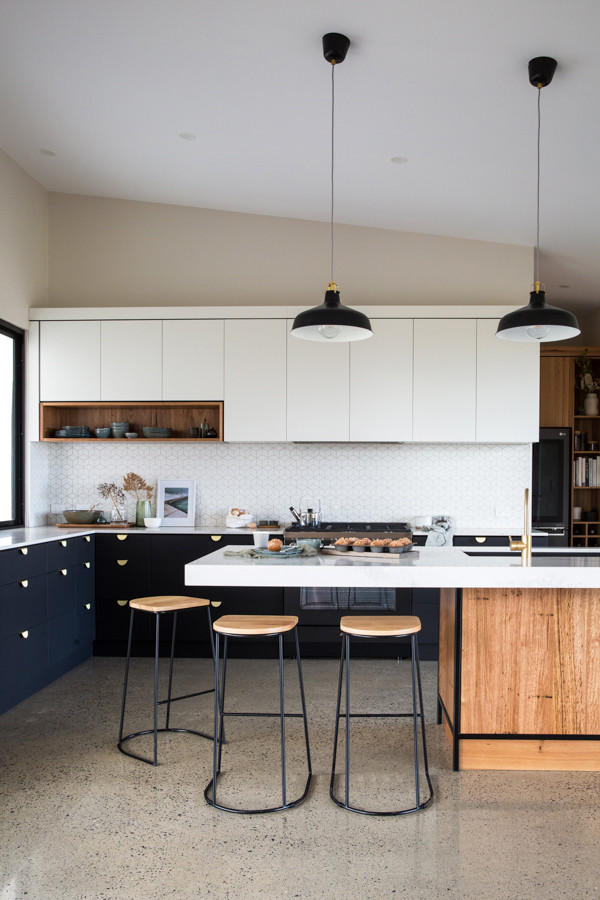 Photo of a large industrial l-shaped kitchen pantry in Other with a single-bowl sink, flat-panel cabinets, black cabinets, solid surface benchtops, white splashback, ceramic splashback, black appliances, concrete floors, with island, grey floor and white benchtop.