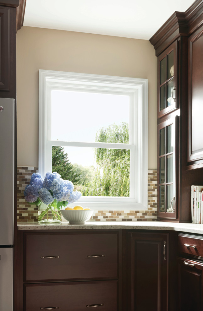 Example of a transitional kitchen design with dark wood cabinets, brown backsplash, stainless steel appliances and beige walls