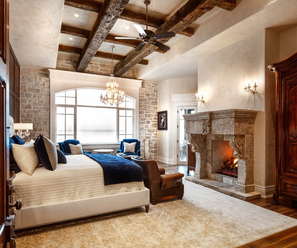 Inspiration for a large traditional master bedroom in Salt Lake City with beige walls, a standard fireplace, a stone fireplace surround, brown floor, exposed beam and wallpaper.