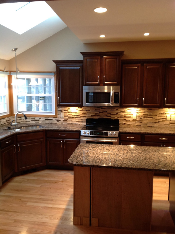 Example of a mid-sized transitional l-shaped light wood floor and beige floor eat-in kitchen design in St Louis with an undermount sink, raised-panel cabinets, dark wood cabinets, granite countertops, multicolored backsplash, matchstick tile backsplash, stainless steel appliances, an island and multicolored countertops
