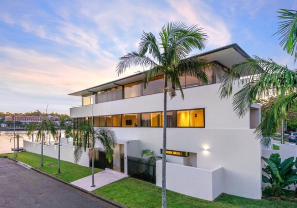 This is an example of a large contemporary three-storey stucco white house exterior in Brisbane with a hip roof, a metal roof and a grey roof.