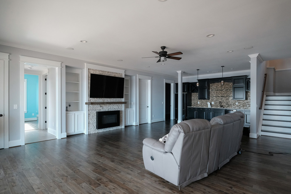 Photo of a large country enclosed family room in DC Metro with a home bar, grey walls, dark hardwood floors, a standard fireplace, a stone fireplace surround, a wall-mounted tv and brown floor.