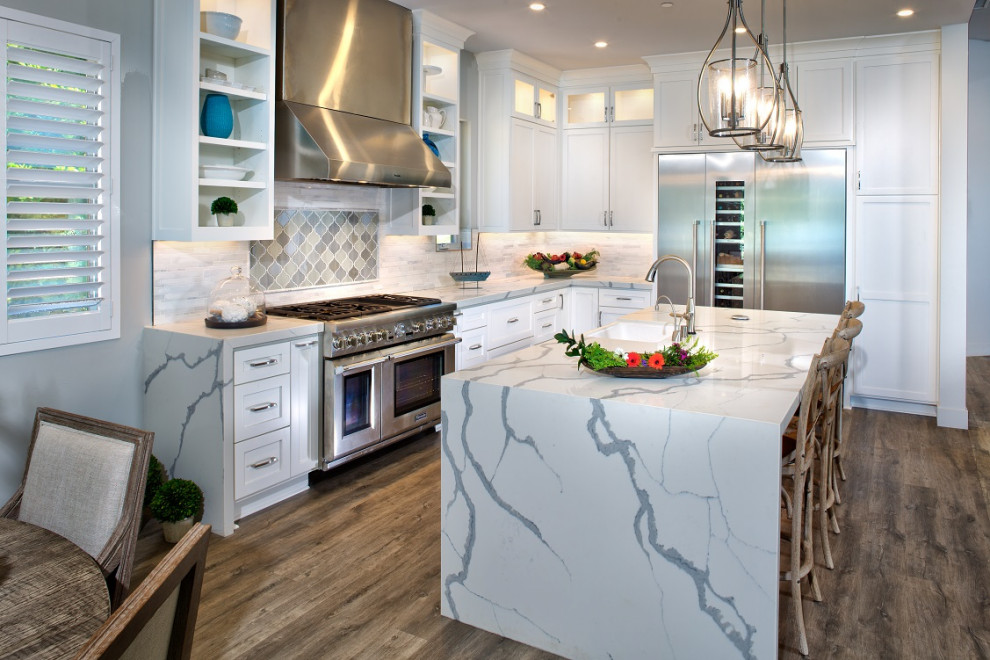 This is an example of a mid-sized transitional l-shaped eat-in kitchen in Sacramento with a farmhouse sink, shaker cabinets, white cabinets, quartz benchtops, white splashback, subway tile splashback, stainless steel appliances, vinyl floors, with island and white benchtop.