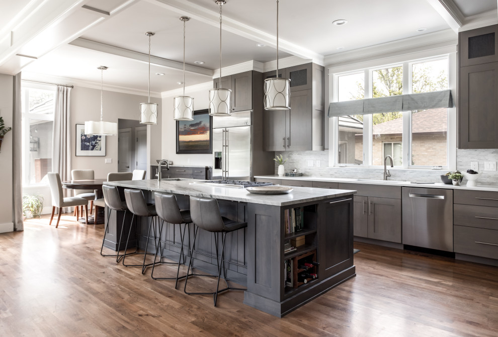 Photo of a transitional galley kitchen in Denver with an undermount sink, shaker cabinets, grey cabinets, grey splashback, mosaic tile splashback, stainless steel appliances, medium hardwood floors, with island, brown floor and white benchtop.