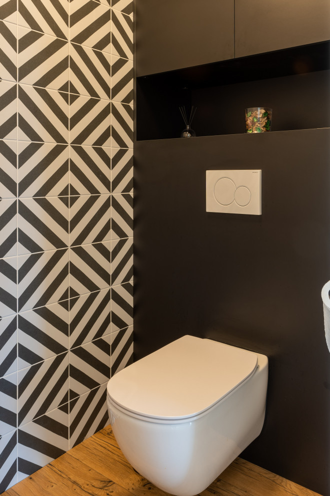 Idée de décoration pour un grand WC suspendu bohème avec un placard à porte affleurante, des portes de placard noires, un carrelage noir et blanc, des carreaux de céramique, un mur noir, sol en stratifié, un lavabo posé, un plan de toilette en bois et meuble-lavabo encastré.