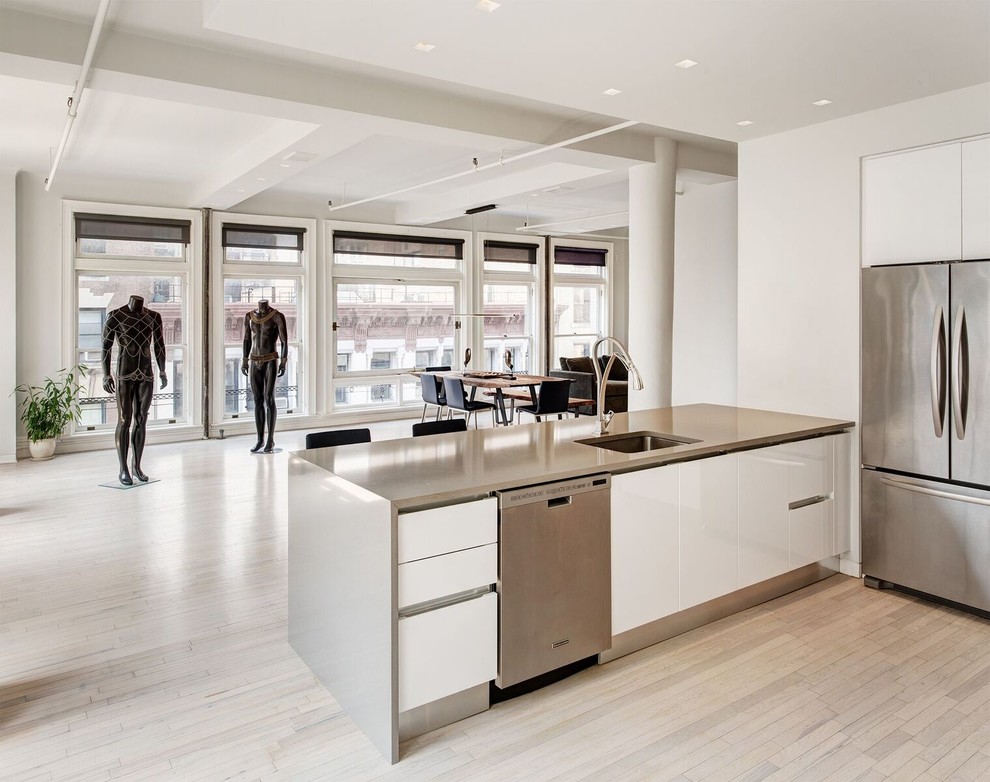 Inspiration for a modern open plan kitchen in New York with an undermount sink, flat-panel cabinets, yellow cabinets, stainless steel benchtops, stainless steel appliances, light hardwood floors and a peninsula.