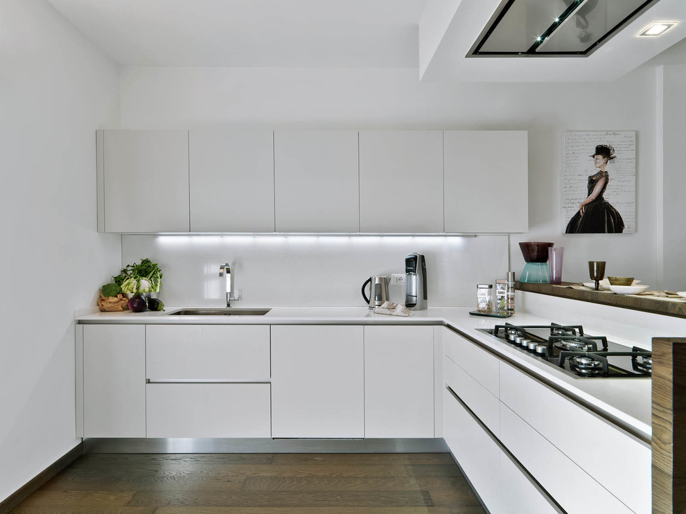 This is an example of a mid-sized contemporary l-shaped open plan kitchen in Milan with an undermount sink, flat-panel cabinets, white cabinets, solid surface benchtops, white splashback and medium hardwood floors.