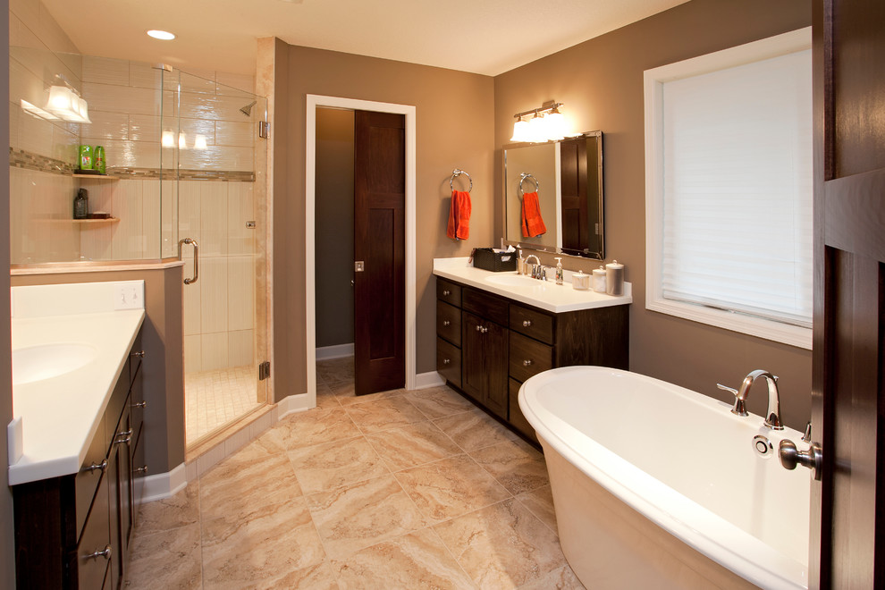Photo of a mid-sized transitional master bathroom in Minneapolis with an integrated sink, furniture-like cabinets, dark wood cabinets, solid surface benchtops, a freestanding tub, a corner shower, beige tile, ceramic tile, brown walls and ceramic floors.