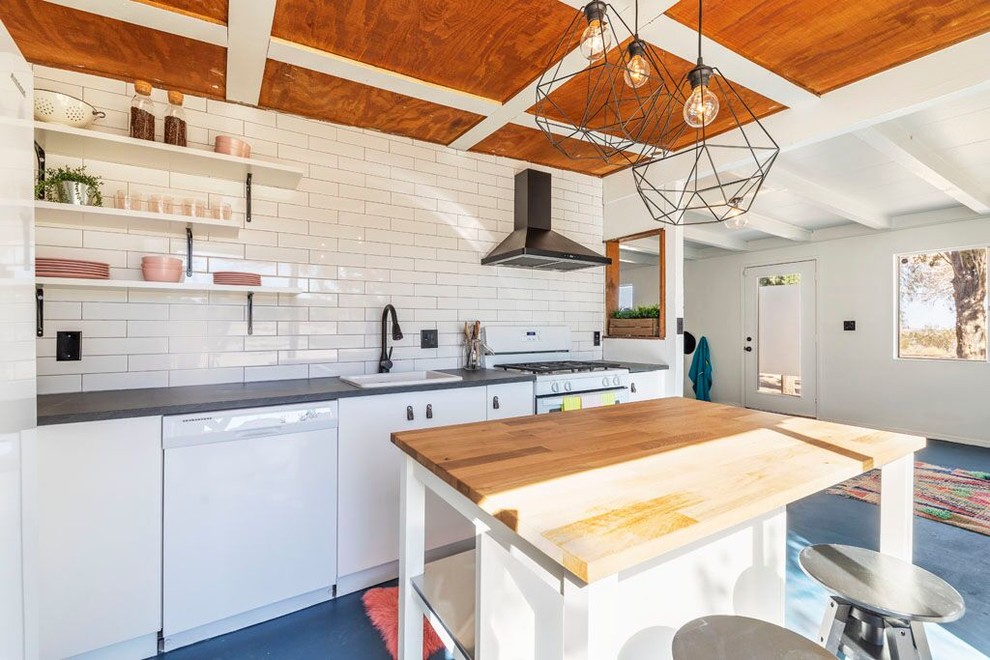 Small contemporary l-shaped open plan kitchen in Other with a drop-in sink, flat-panel cabinets, white cabinets, white splashback, white appliances, concrete floors, with island, blue floor, grey benchtop, zinc benchtops and subway tile splashback.