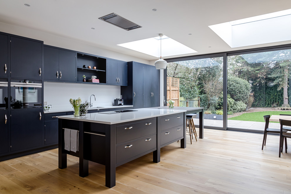 Design ideas for a large contemporary l-shaped eat-in kitchen in London with a single-bowl sink, blue cabinets, medium hardwood floors, brown floor, shaker cabinets, white splashback and with island.