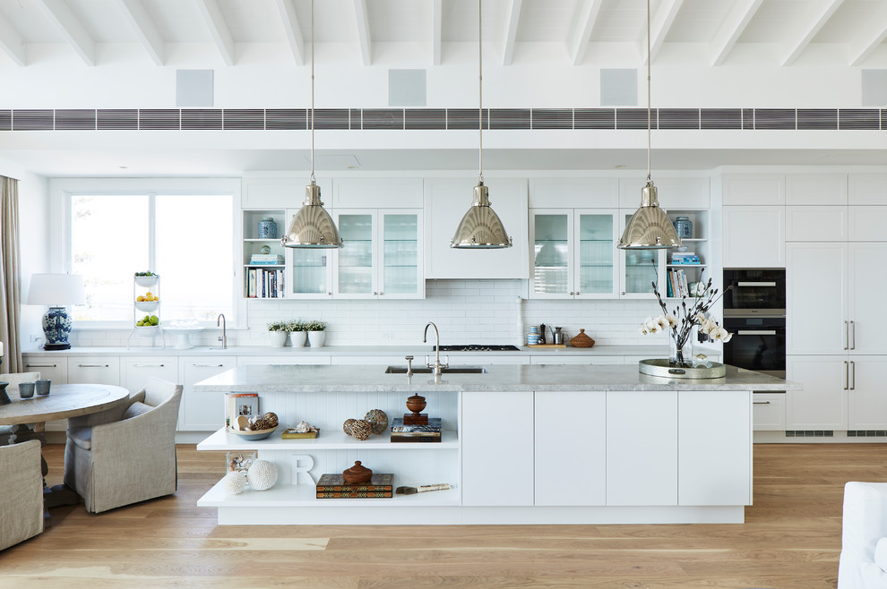 Inspiration for a large beach style single-wall open plan kitchen in Sydney with shaker cabinets, white cabinets, quartz benchtops, white splashback, ceramic splashback, with island and grey benchtop.