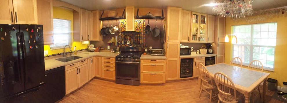 Photo of a mid-sized modern l-shaped open plan kitchen in New York with shaker cabinets, light wood cabinets, multi-coloured splashback, glass tile splashback, black appliances, light hardwood floors and no island.