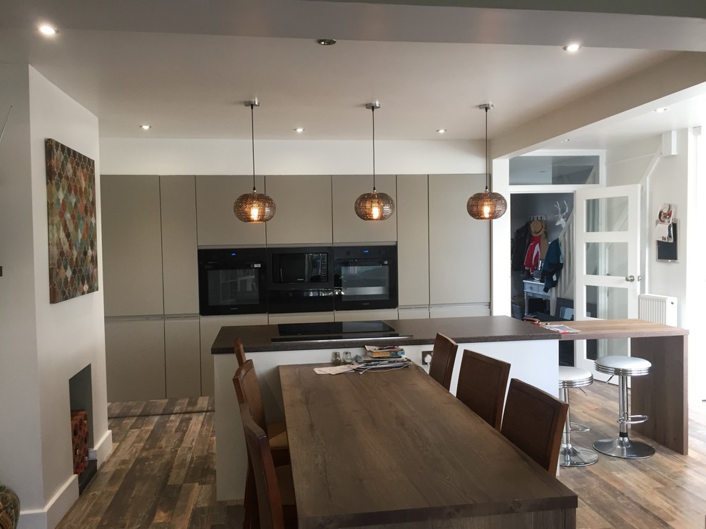 Inspiration for a mid-sized contemporary single-wall eat-in kitchen in Other with an undermount sink, flat-panel cabinets, brown cabinets, wood benchtops, black appliances, vinyl floors, with island, brown floor and multi-coloured benchtop.