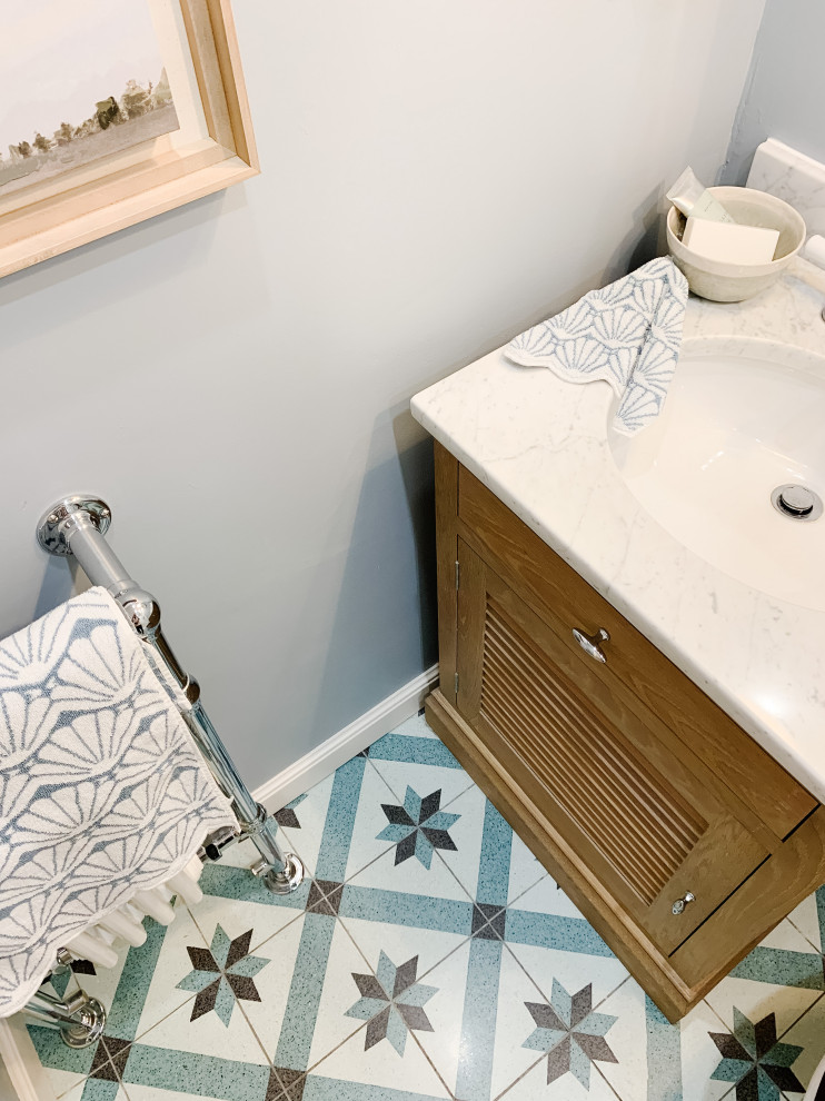 Exemple d'une petite salle d'eau chic avec un placard à porte persienne, des portes de placard marrons, une douche ouverte, WC à poser, un carrelage blanc, mosaïque, un mur bleu, un sol en terrazzo, un lavabo posé, un plan de toilette en marbre, un sol multicolore, une cabine de douche à porte battante, un plan de toilette blanc, meuble simple vasque, meuble-lavabo sur pied et du lambris.
