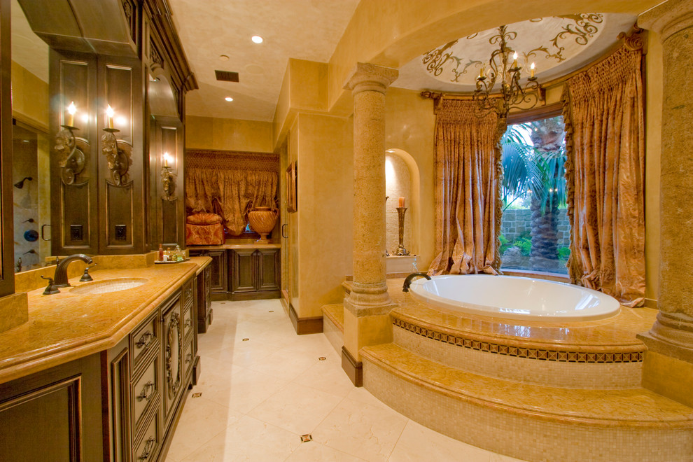 Photo of a mediterranean bathroom in Los Angeles with dark wood cabinets, beige tile and a drop-in tub.