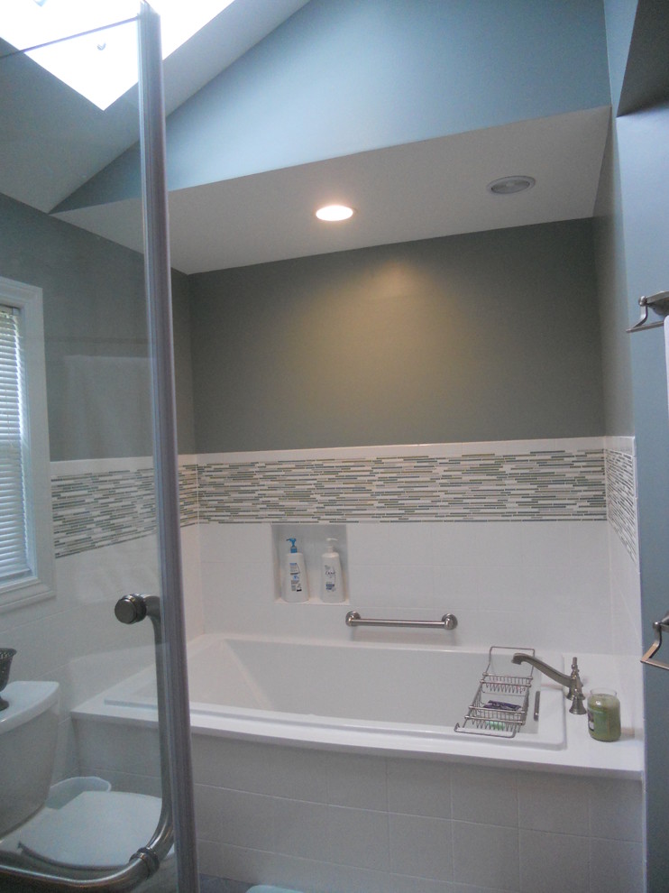 Example of a large transitional master gray tile and stone tile ceramic tile corner bathtub design with an undermount sink, recessed-panel cabinets, dark wood cabinets, quartz countertops, a two-piece toilet and gray walls