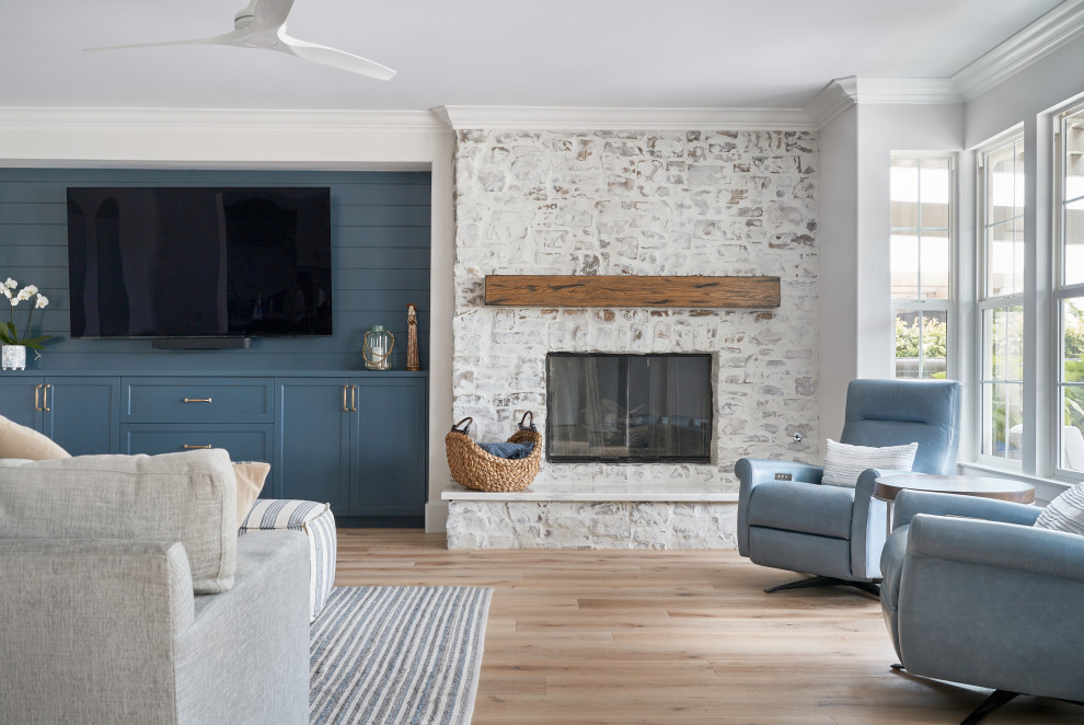 Modelo de salón abierto clásico renovado grande con paredes azules, suelo de madera clara, todas las chimeneas, marco de chimenea de ladrillo, televisor colgado en la pared, suelo beige y machihembrado