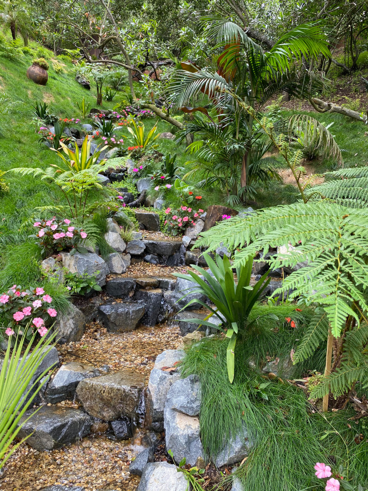 Aménagement d'un grand jardin à la française arrière asiatique l'été avec une cascade, une exposition partiellement ombragée et des galets de rivière.