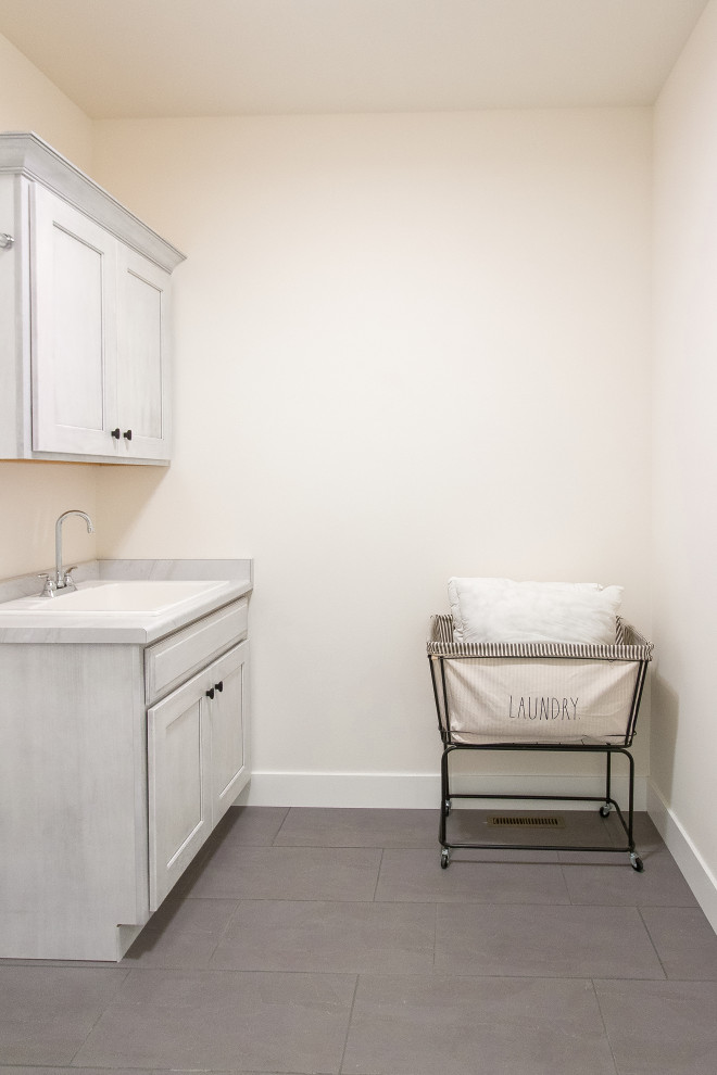 Example of a transitional single-wall ceramic tile and gray floor dedicated laundry room design with recessed-panel cabinets, white cabinets, laminate countertops and white walls