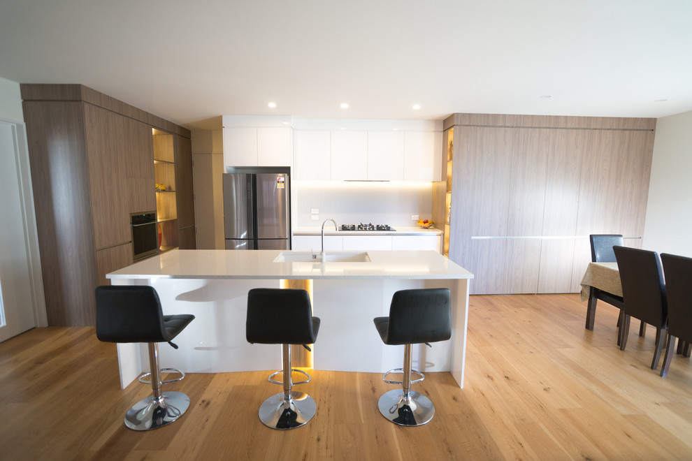 Design ideas for a large contemporary galley eat-in kitchen in Christchurch with an undermount sink, white cabinets, quartz benchtops, white splashback, glass sheet splashback, stainless steel appliances, laminate floors, with island and brown floor.