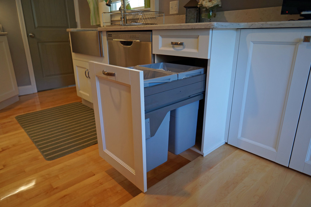 Example of a large transitional l-shaped light wood floor eat-in kitchen design in Boston with a farmhouse sink, shaker cabinets, white cabinets, quartz countertops, white backsplash, stone slab backsplash, stainless steel appliances and an island