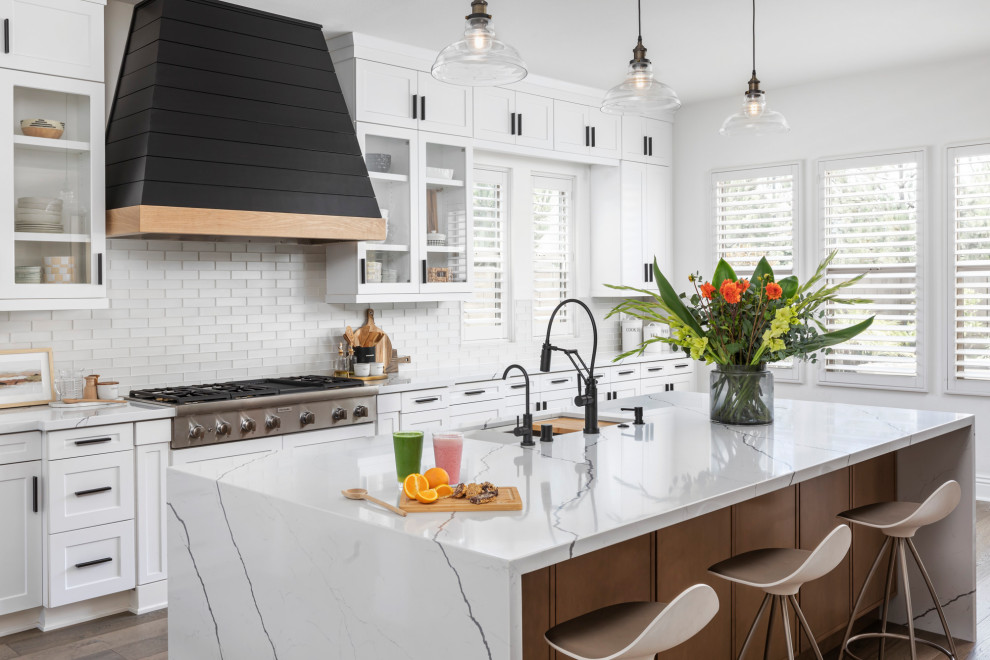 Small modern galley open plan kitchen in Orange County with a farmhouse sink, shaker cabinets, white cabinets, quartzite benchtops, white splashback, glass tile splashback, stainless steel appliances, dark hardwood floors, with island, brown floor and white benchtop.