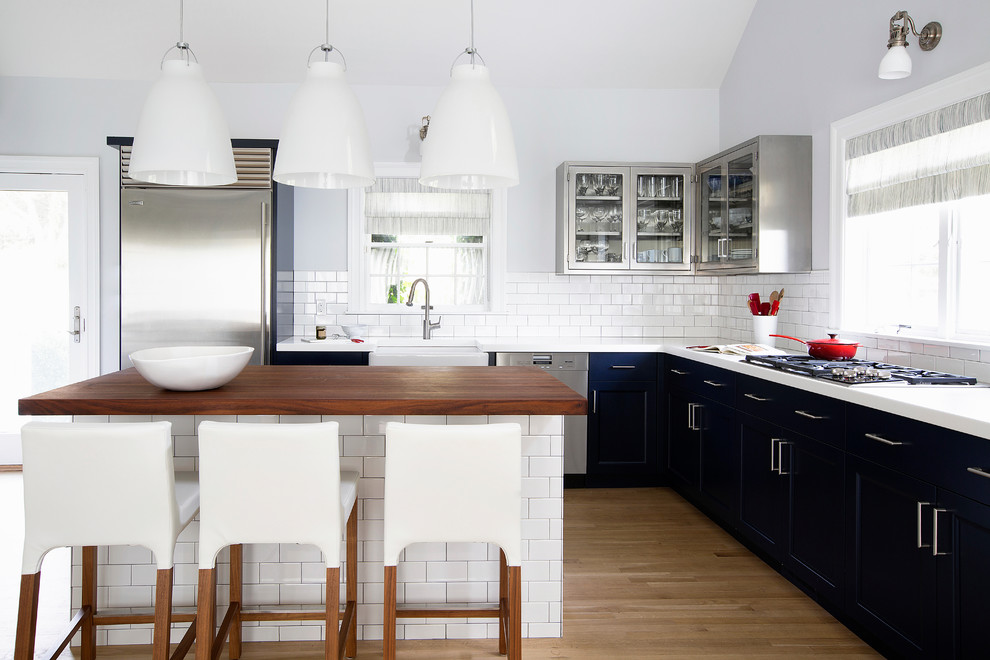 Inspiration for a mid-sized contemporary l-shaped kitchen in New York with a farmhouse sink, shaker cabinets, blue cabinets, white splashback, subway tile splashback, stainless steel appliances, light hardwood floors and with island.