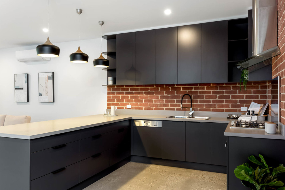 Photo of a mid-sized contemporary u-shaped open plan kitchen in Adelaide with flat-panel cabinets, black cabinets, quartz benchtops, red splashback, brick splashback, black appliances, concrete floors, grey floor, grey benchtop, a drop-in sink and a peninsula.