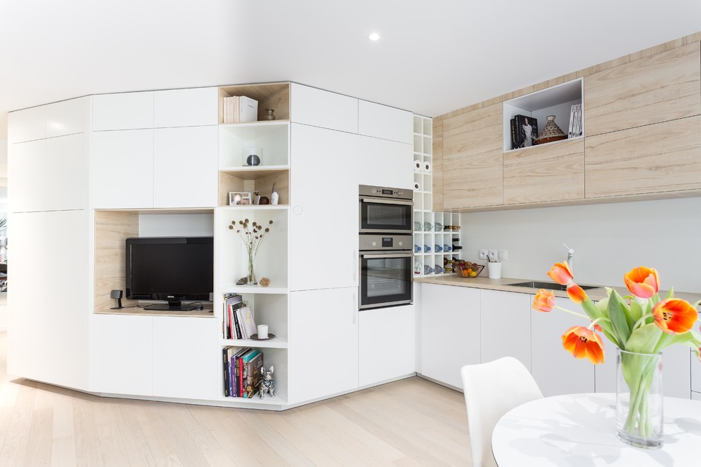 Mid-sized scandinavian l-shaped open plan kitchen in Paris with a single-bowl sink, flat-panel cabinets, white cabinets, laminate benchtops, white splashback, glass sheet splashback, stainless steel appliances, light hardwood floors and no island.