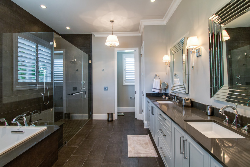 This is an example of a large contemporary master bathroom in Charleston with shaker cabinets, grey cabinets, a drop-in tub, a curbless shower, a one-piece toilet, brown tile, porcelain tile, grey walls, porcelain floors, an undermount sink, engineered quartz benchtops, brown floor and a hinged shower door.
