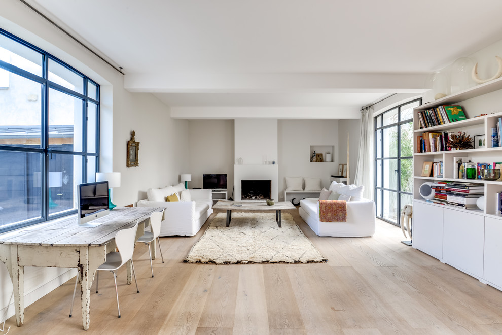 Photo of a large contemporary open concept family room in Paris with a library, white walls, light hardwood floors, a standard fireplace, a freestanding tv, a plaster fireplace surround and white floor.