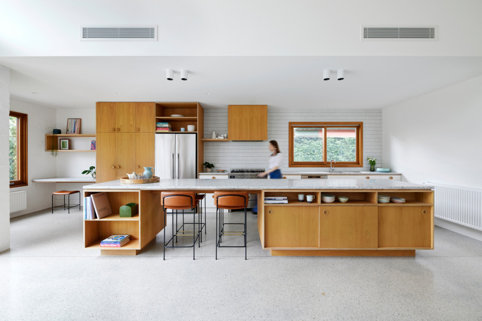 This is an example of a large midcentury galley kitchen in Melbourne with a single-bowl sink, flat-panel cabinets, light wood cabinets, terrazzo benchtops, white splashback, mosaic tile splashback, stainless steel appliances, concrete floors, with island, grey floor and grey benchtop.