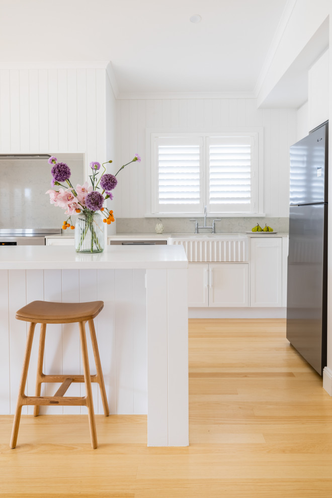 Photo of a mid-sized beach style l-shaped eat-in kitchen in Townsville with shaker cabinets, white cabinets, quartz benchtops, light hardwood floors, with island and white benchtop.