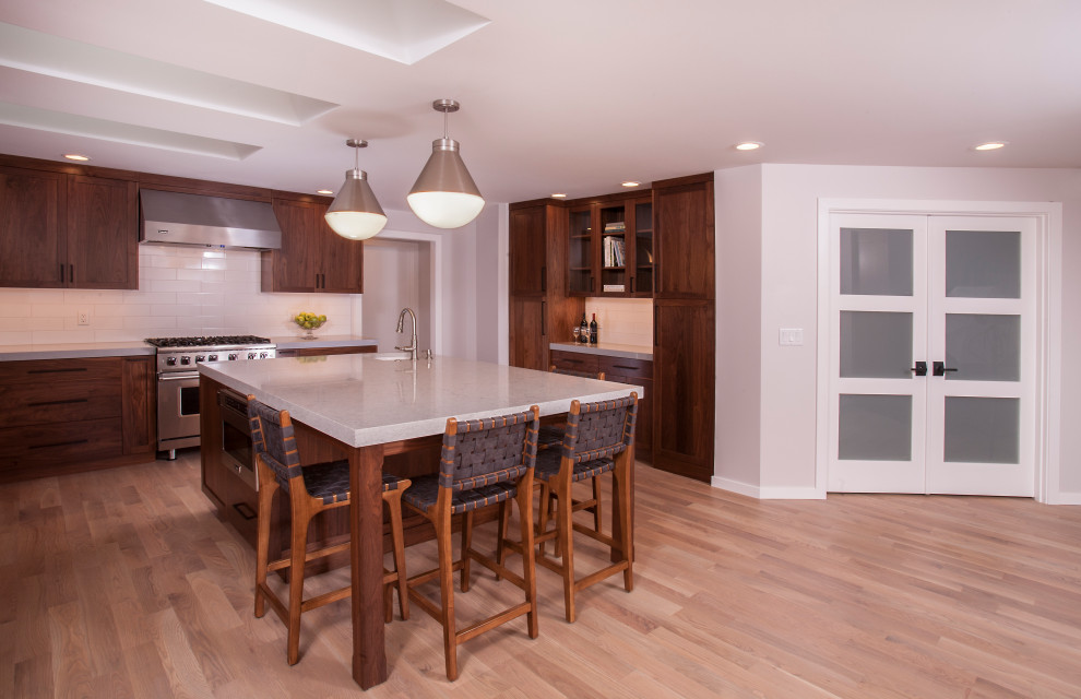 Large transitional u-shaped light wood floor and brown floor eat-in kitchen photo in Seattle with a farmhouse sink, dark wood cabinets, white backsplash, subway tile backsplash, stainless steel appliances, an island and white countertops