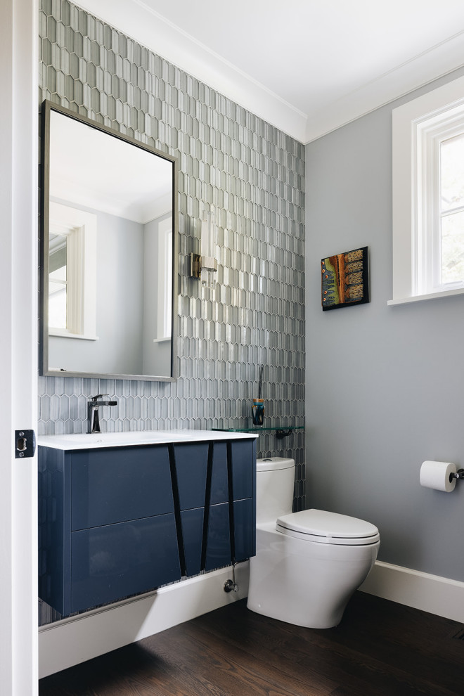 This is an example of a transitional powder room in Chicago with blue cabinets, a one-piece toilet, gray tile, ceramic tile, grey walls, dark hardwood floors, brown floor, white benchtops and a floating vanity.