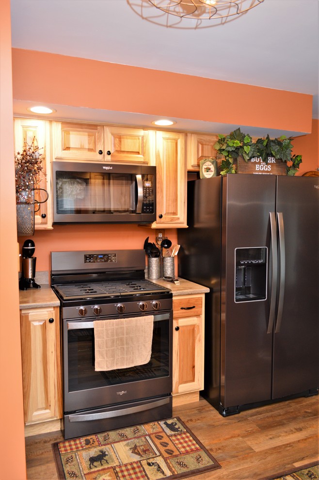 This is an example of a mid-sized country u-shaped eat-in kitchen in Other with an undermount sink, raised-panel cabinets, light wood cabinets, solid surface benchtops, stainless steel appliances, laminate floors, a peninsula, brown floor and brown benchtop.