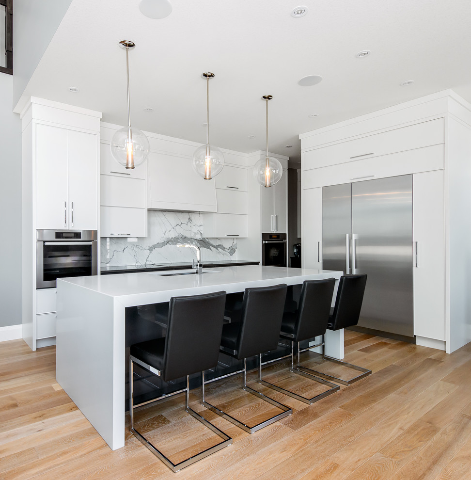 Photo of a mid-sized contemporary l-shaped eat-in kitchen in Calgary with flat-panel cabinets, white cabinets, white splashback, stone slab splashback, panelled appliances, with island, an undermount sink, quartz benchtops, light hardwood floors and brown floor.
