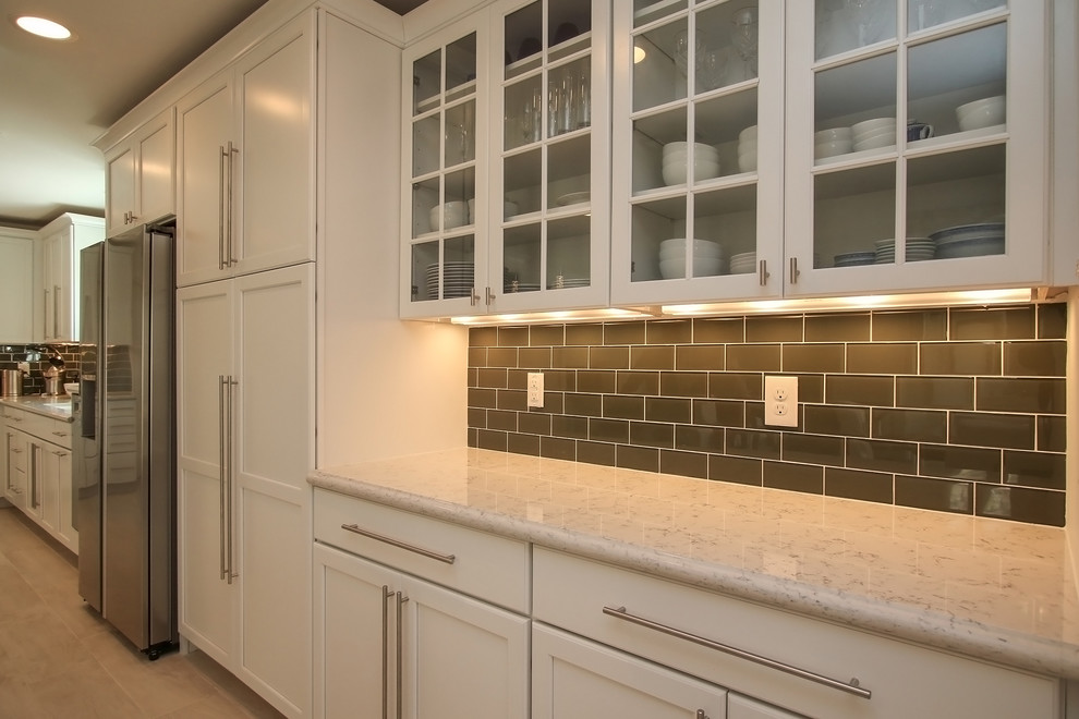 This is an example of a transitional kitchen in Houston with an undermount sink, recessed-panel cabinets, white cabinets, quartz benchtops, green splashback, glass tile splashback, stainless steel appliances, light hardwood floors and a peninsula.
