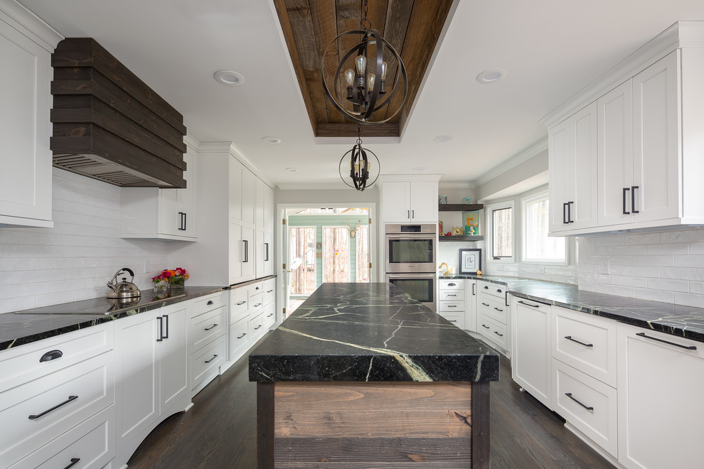 Design ideas for a country kitchen in Raleigh with shaker cabinets, white cabinets, white splashback, subway tile splashback, panelled appliances, dark hardwood floors, with island, brown floor and black benchtop.