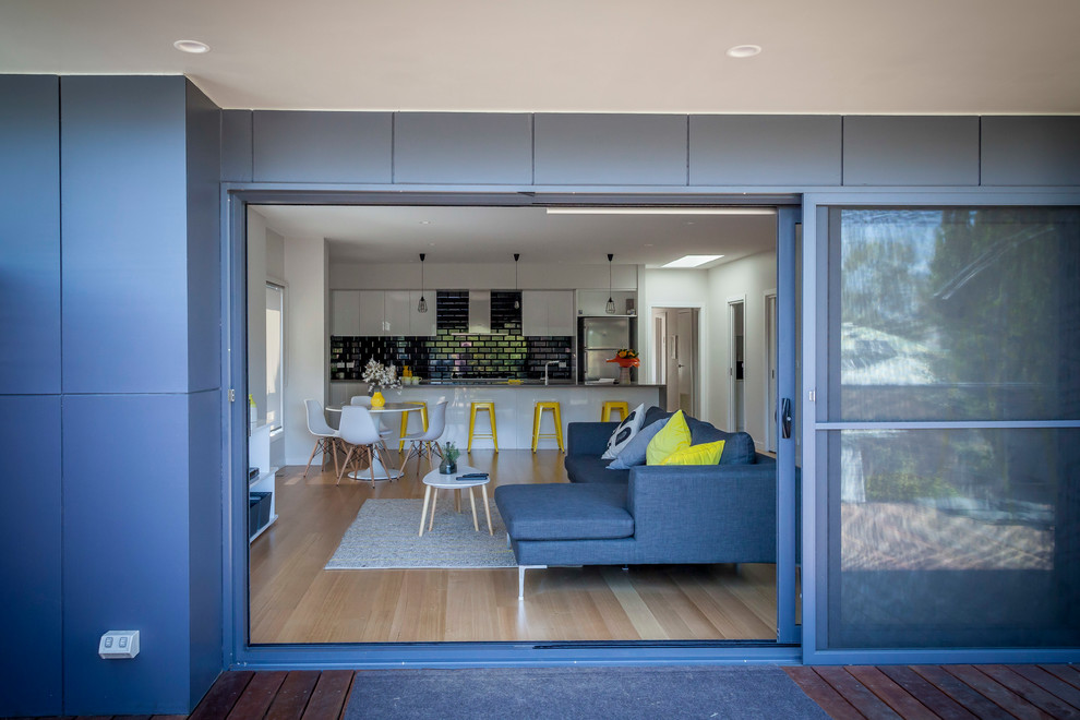 This is an example of a mid-sized contemporary open concept family room in Melbourne with white walls, medium hardwood floors and a freestanding tv.