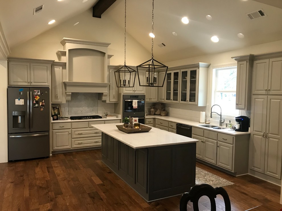 Example of a large transitional l-shaped dark wood floor and brown floor open concept kitchen design with raised-panel cabinets, an island, a double-bowl sink, gray cabinets, white backsplash, subway tile backsplash, stainless steel appliances and white countertops