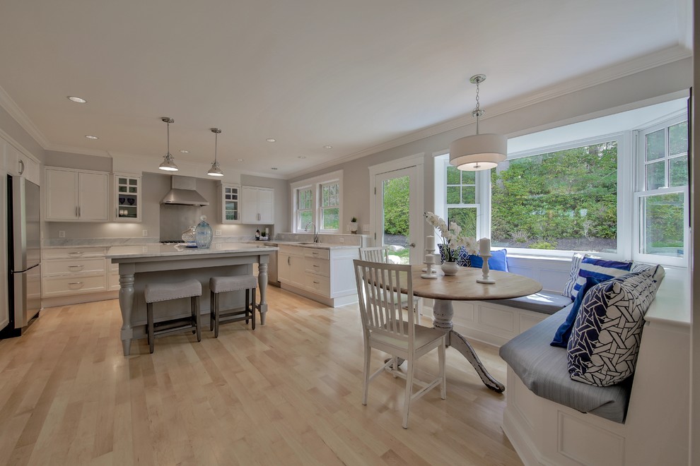 Inspiration for a large beach style u-shaped separate kitchen in Boston with an undermount sink, shaker cabinets, marble benchtops, white splashback, stainless steel appliances, light hardwood floors and with island.