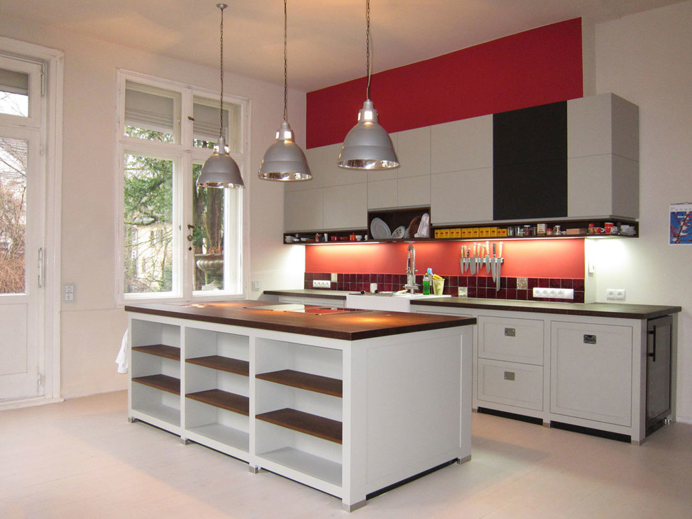 Design ideas for a large contemporary single-wall open plan kitchen in Berlin with a farmhouse sink, flat-panel cabinets, white cabinets, wood benchtops, red splashback, painted wood floors, with island and ceramic splashback.