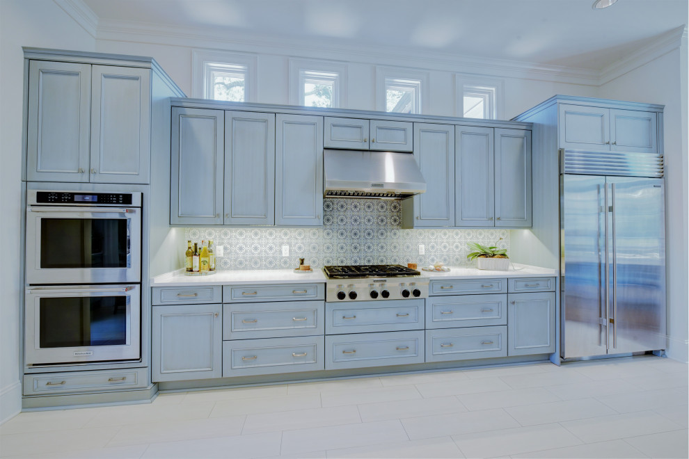 This is an example of a large traditional galley eat-in kitchen in New Orleans with a farmhouse sink, recessed-panel cabinets, blue cabinets, solid surface benchtops, multi-coloured splashback, ceramic splashback, stainless steel appliances, a peninsula, grey floor and white benchtop.