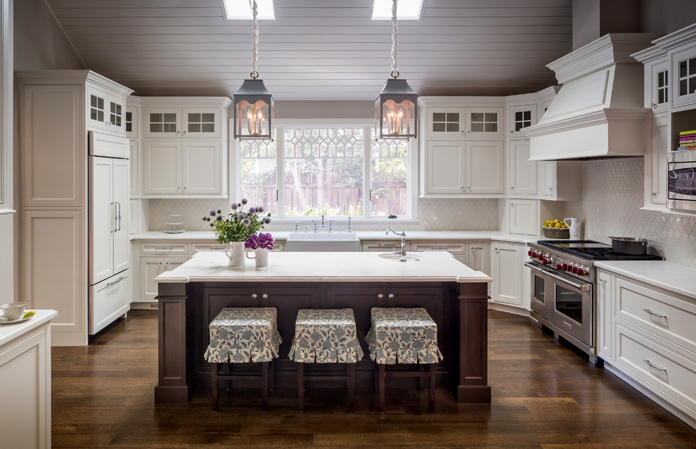 This is an example of a traditional u-shaped kitchen in San Francisco with a farmhouse sink, recessed-panel cabinets, white cabinets, white splashback, stainless steel appliances, dark hardwood floors, with island and brown floor.