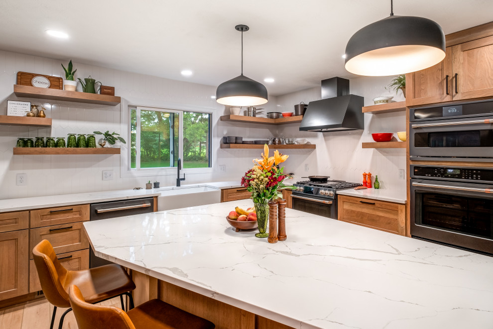 This is an example of a mid-sized transitional l-shaped eat-in kitchen in Other with a farmhouse sink, shaker cabinets, medium wood cabinets, quartz benchtops, white splashback, porcelain splashback, black appliances, vinyl floors, with island, beige floor and white benchtop.
