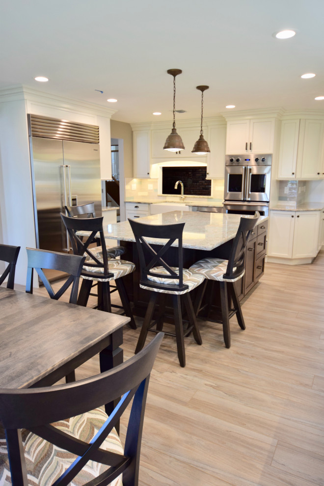 Example of a huge transitional vinyl floor and brown floor eat-in kitchen design with a farmhouse sink, recessed-panel cabinets, white cabinets, quartz countertops, multicolored backsplash, ceramic backsplash, stainless steel appliances, an island and multicolored countertops