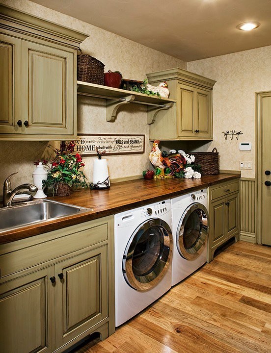 Traditional single-wall laundry room in Other with a drop-in sink, raised-panel cabinets, green cabinets, wood benchtops, beige walls, light hardwood floors, a side-by-side washer and dryer and brown benchtop.