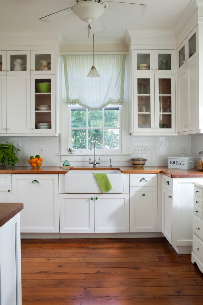 Traditional kitchen in Wilmington with glass-front cabinets, a farmhouse sink, wood benchtops, white cabinets, white splashback and subway tile splashback.