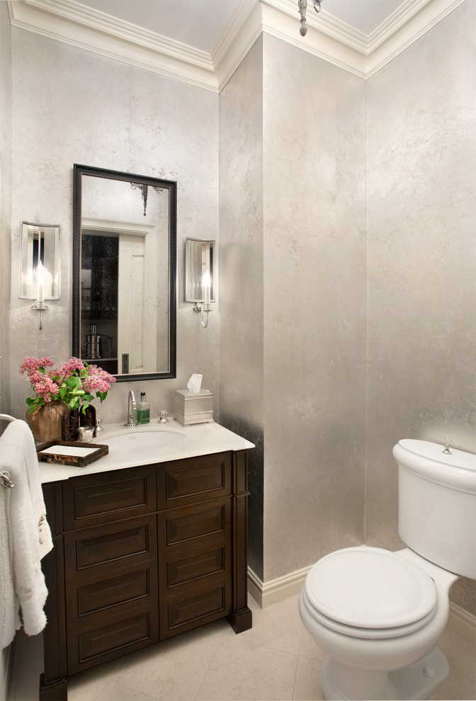 Small traditional powder room in New York with an undermount sink, raised-panel cabinets, brown cabinets, marble benchtops, a two-piece toilet, beige tile, grey walls and limestone floors.